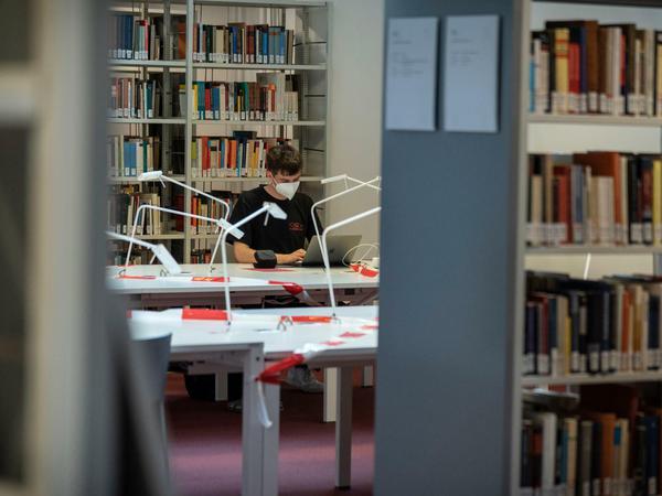 Ein Student sitzt mit FFP2-Maske in einem Bibliotheksraum der Freien Universität Berlin am Laptop.