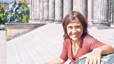 Eine Frau sitzt vor einem Museumsbau in der Sonne und lächelt.