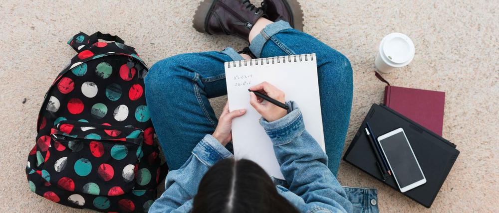 Eine Studentin sitzt im Schneidersitz am Boden und schreibt in einen Collegeblock.