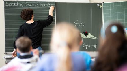 Eine Grundschullehrerin schreibt Wörter an eine Tafel, die Kinder folgen dem Unterricht.