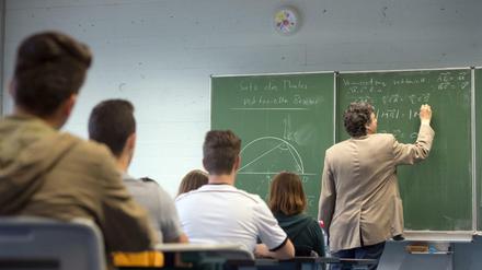 Ein Mathelehrer steht an der Tafel, die Schüler hören zu.