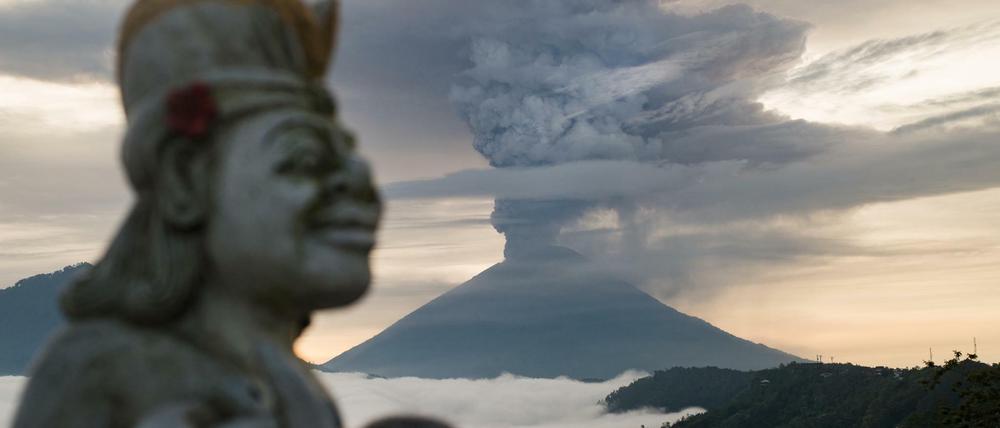 Eine Statue ist neben der riesigen Rauchsäule über dem Vulkan Mount Agung zu sehen.