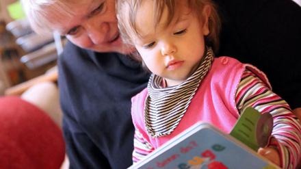 Eine ältere Frau liest einem Kleinkind aus einem Buch vor.