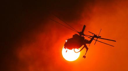 Ein Feuerwehrhubschrauber fliegt in Griechenland vor der Sonne zu einem Waldbrand.